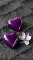 Fototapeta premium Two shiny purple heart shapes beside a delicate flower