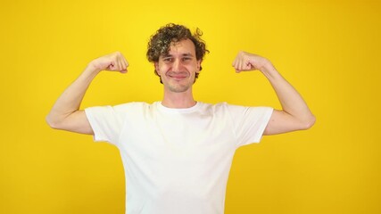 Confident young man flexes his biceps with a cheerful smile on a vibrant yellow studio background perfect for fitness branding, motivational campaigns, lifestyle marketing, and International Men's Day