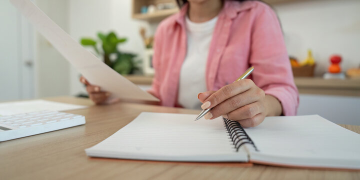 Work from Home. Woman taking notes while reviewing documents at desk.