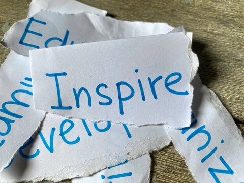A close-up of the word "Inspire" clearly written in blue handwriting on a torn piece of white paper, conveying a message of encouragement.