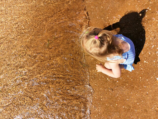 Little girl playing in wet sand on the coast of calm sea on sunny day, view from above