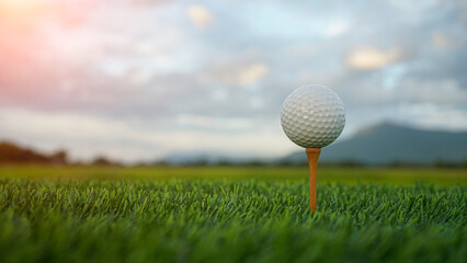 Golf Ball on Tee in Lush Green Grass Under Cloudy Sky at Sunset