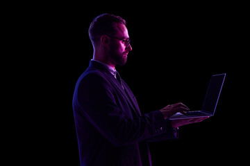Man in dark suit using laptop in neon lighting against black background. Concept of UX platform...