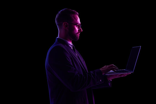 Man in dark suit using laptop in neon lighting against black background. Concept of UX platform navigation, corporate SaaS demo visuals, and future-of-money workplace mobility.