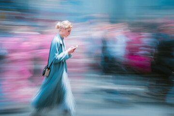 Young woman walking while checking her phone in blurred city scene  