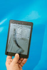 Hand holding broken and water-damaged tablet with shattered screen close-up, weak device protection against impact and moisture, water-damaged tablet