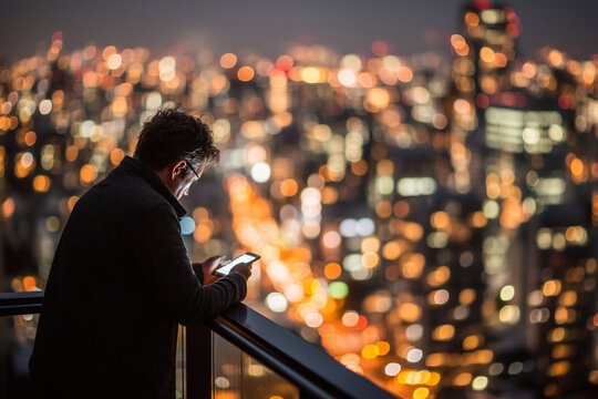 Man using smartphone on balcony overlooking city skyline at night  