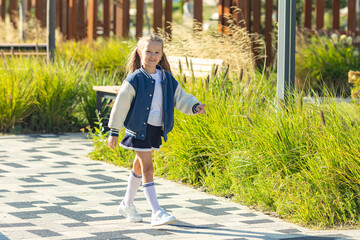Little school girl wearing a skirt and blue bomber jacket enjoys a sunny day walking and having fun...