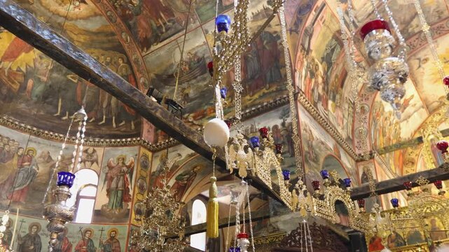 Explore the detailed frescoes and ornate chandeliers inside Bachkovo Monastery. The warm lighting highlights the intricate artwork, creating a serene, historical ambiance.