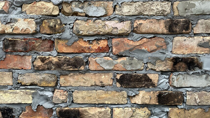 Horizontal vintage brick wall made of scorched reclaimed bricks with rough cement and soot stains