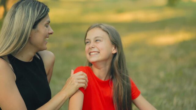 Playful mother whispers to smiling daughter on a cozy park afternoon