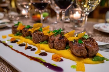 An exquisite presentation of gourmet steak medallions served with a vibrant yellow puree, artistic sauces, and garnished with microgreens, set against a backdrop of wine glasses.