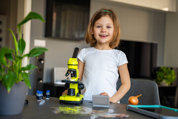 Little girl examining onion skin under a microscope. Concept of early science education and cell structure exploration
