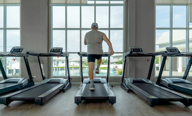 A man walking on a treadmill in the gym. Stand facing large window, enjoy view of a pool outside. The bright sunlight fill the fitness area, creating an inviting atmosphere for exercise.