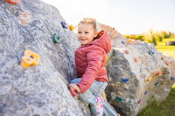 Little girl climbing an artificial climbing wall in a playground, developing strength and coordination