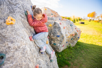 Little girl climbing an artificial climbing wall in a playground, developing strength and coordination