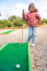 Little girl playing mini golf outdoor. Child having fun with new activity in spring time. Family vacations or resort.