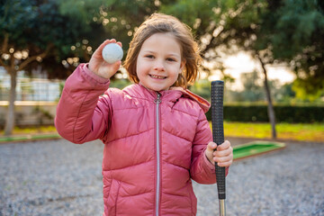 Portrait of Little girl Holding in hand Mini-Golf Ball. Little girl playing mini golf outdoor. Family vacations or resort.