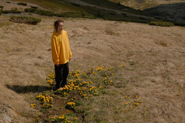 Woman in Yellow Jacket Standing Among Wildflowers in Mountainous Landscape