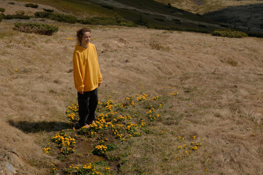 Woman in Yellow Jacket Standing Among Wildflowers in Mountainous Landscape