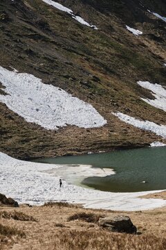Solitary Hiker at Alpine Lake in Snowy Mountain Landscape