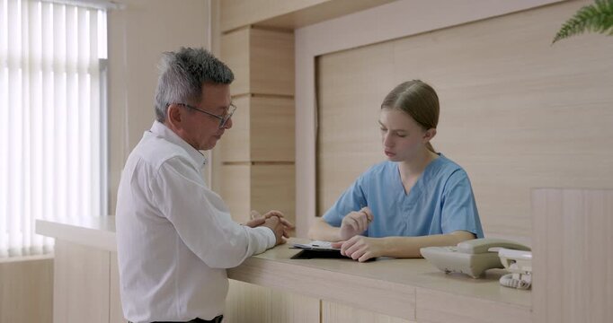 Slowmotion scene of hospital billing interaction with asian male preparing credit card payment while young female nurse handling medical charge process at reception counter