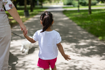 Mother walking with daughter, small dog trotting alongside during sunny park outing