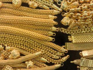 An extensive array of intricate gold bracelet  is meticulously arranged on a dark surface,...
