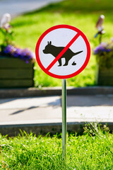 Sign pole on green grass warning against walking dogs and leaving pet waste on urban lawns in city park area, public cleanliness and rules, no dog walking allowed on grassy public lawns in the city