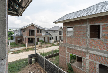 Newly built house line a quiet road in a developing suburban neighborhood. Construction is ongoing, with clear skies overhead and greenery surrounding the area, reflecting a growing community.