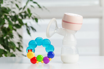 Baby care. Breast pump with milk and colorful baby rattle.