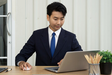 A professional man in a suit sit at a wooden table in a contemporary office, focused on laptop computer.