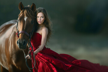 Elegant Woman in a Red Dress Poses With a Brown Horse During Golden Hour in a Picturesque Outdoor Setting