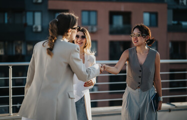 A group of businesswomen meeting and greeting on a rooftop terrace during sunset, showcasing...