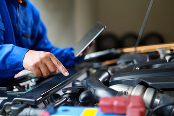 Mechanic standing inspecting car with laptop checking performance and operation of car. Maintenance topic for service, vehicle check up, customer service.