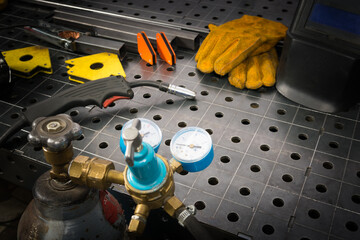 On a metal table there is a set of tools for gas welding, in the middle there is a place for an inscription, gloves and mask, magnets