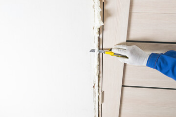 hand holds a knife and cuts off the mounting foam from the door frame after installation, close-up