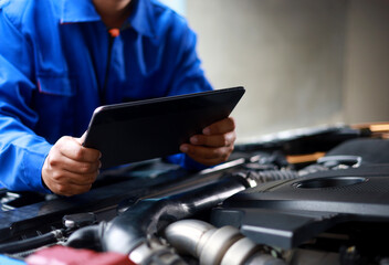 Mechanic standing inspecting car with laptop checking performance and operation of car. Maintenance topic for service, vehicle check up, customer service.
