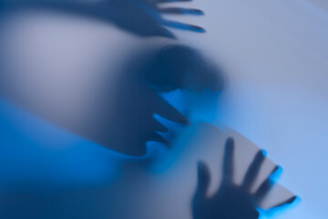Abstract Silhouette of Hands and Face Behind Blue-Toned Fabric
