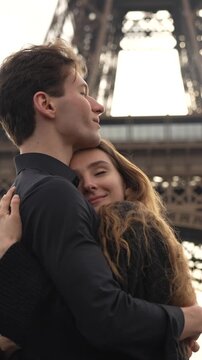 Romantic couple lovingly embracing beneath the Eiffel Tower in Paris on a sunny day