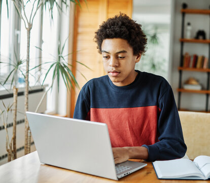Portrait of teenage black boy using laptop computer at home. Teenage boy attending to online school class