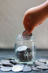 Hand holding a coin put in a jar on a table, Saving money concept