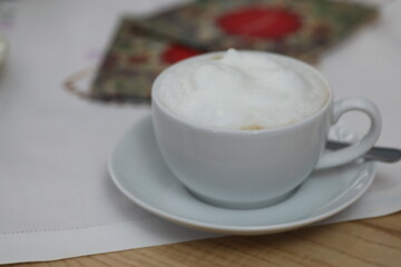 White coffee cup with foam on top sits on a white saucer