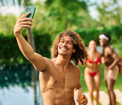 Young people having fun dancing and drinking and bonding listening to music at a party by pool in a villa or resort, Young people enjoying vacation in a tropical resort hotel, young man dancing and ta - Powered by Adobe