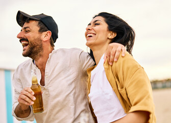 Group of young cheerful people, happy couple in front,  having fun walking and drinking beer at the...