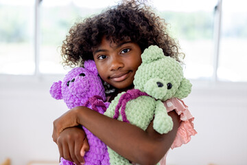 cheerful african american child playing with teddy bear in living room. African american girl hug...