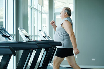 An overweight man running on a treadmill while exercising at the gym.