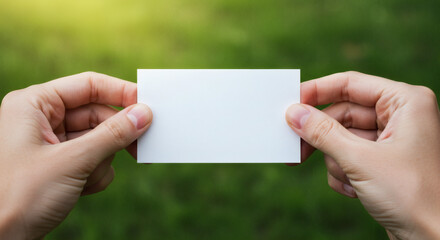 Blank business card held in hands against a blurred green background.
