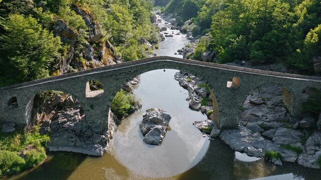 Aerial view of Devil&rsquo;s Bridge, curved stone structure crossing Arda River in Bulgaria Rhodopes surrounded by rocky cliffs green forest in summer, perfect for tourism, adventure history theme travel