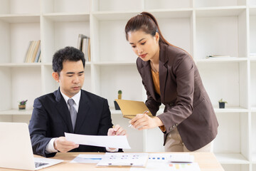 Two Asian business people with analyzing financial report working together in office.